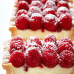 Cheesecake tart with fresh raspberries, creamy filling and flaky crust, dusted with powdered sugar.