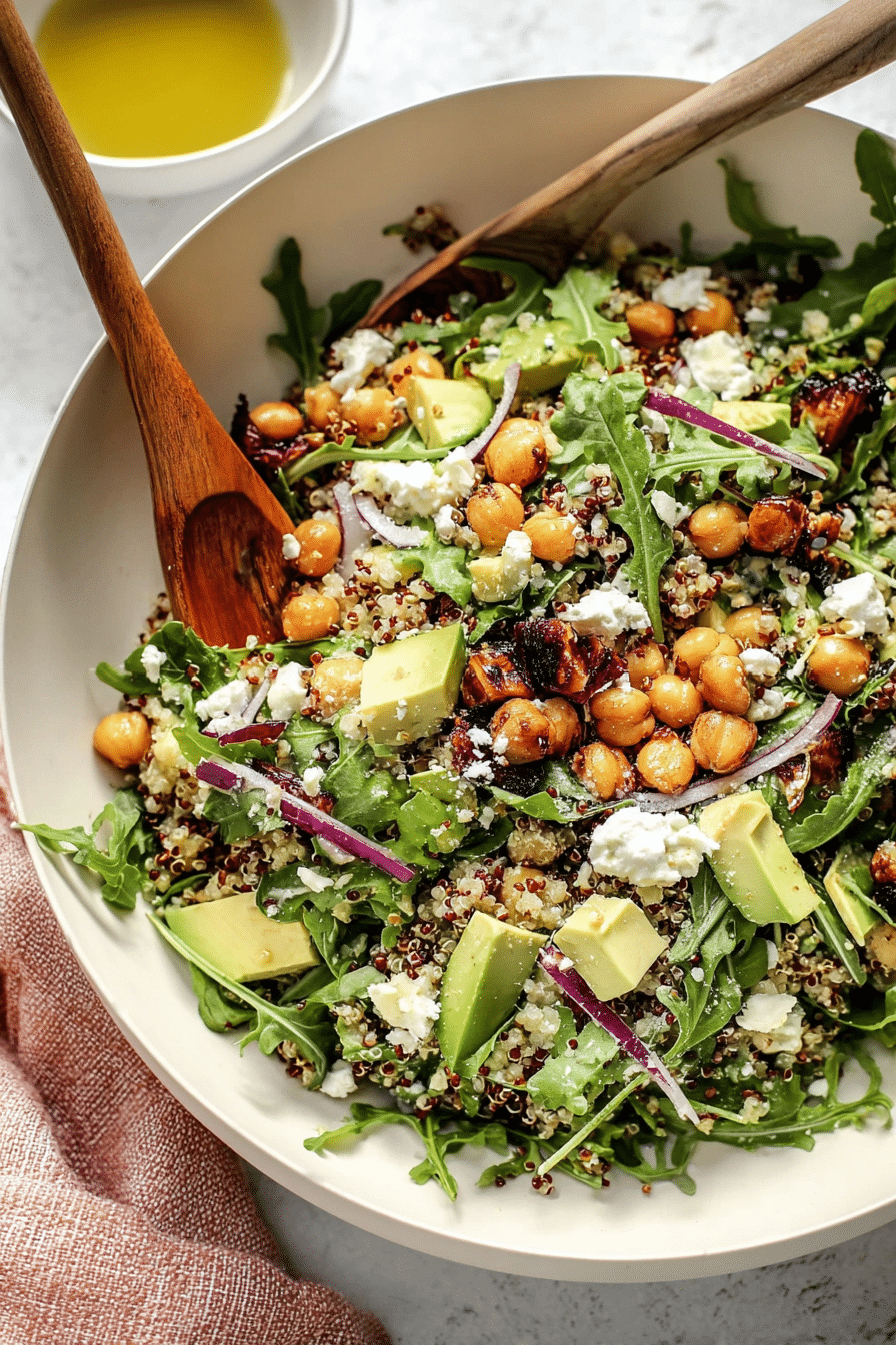 A colorful chickpea arugula quinoa salad with feta, avocado, and dates on a wooden table.