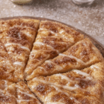 Delicious cinnamon pizza topped with glaze, ready to be sliced in a cozy kitchen.