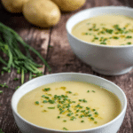 Delicious bowl of classic potato leek soup garnished with fresh chives and served with a wooden spoon.