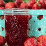 Close-up of a jar of classic strawberry jam surrounded by fresh strawberries on a rustic wooden table.