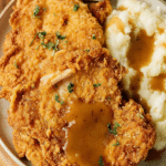 Delicious country fried chicken served with creamy mashed potatoes and rich gravy, perfect for a family dinner.