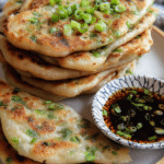 Crispy Chinese scallion pancakes stacked on a plate with scallion garnish and dipping sauce