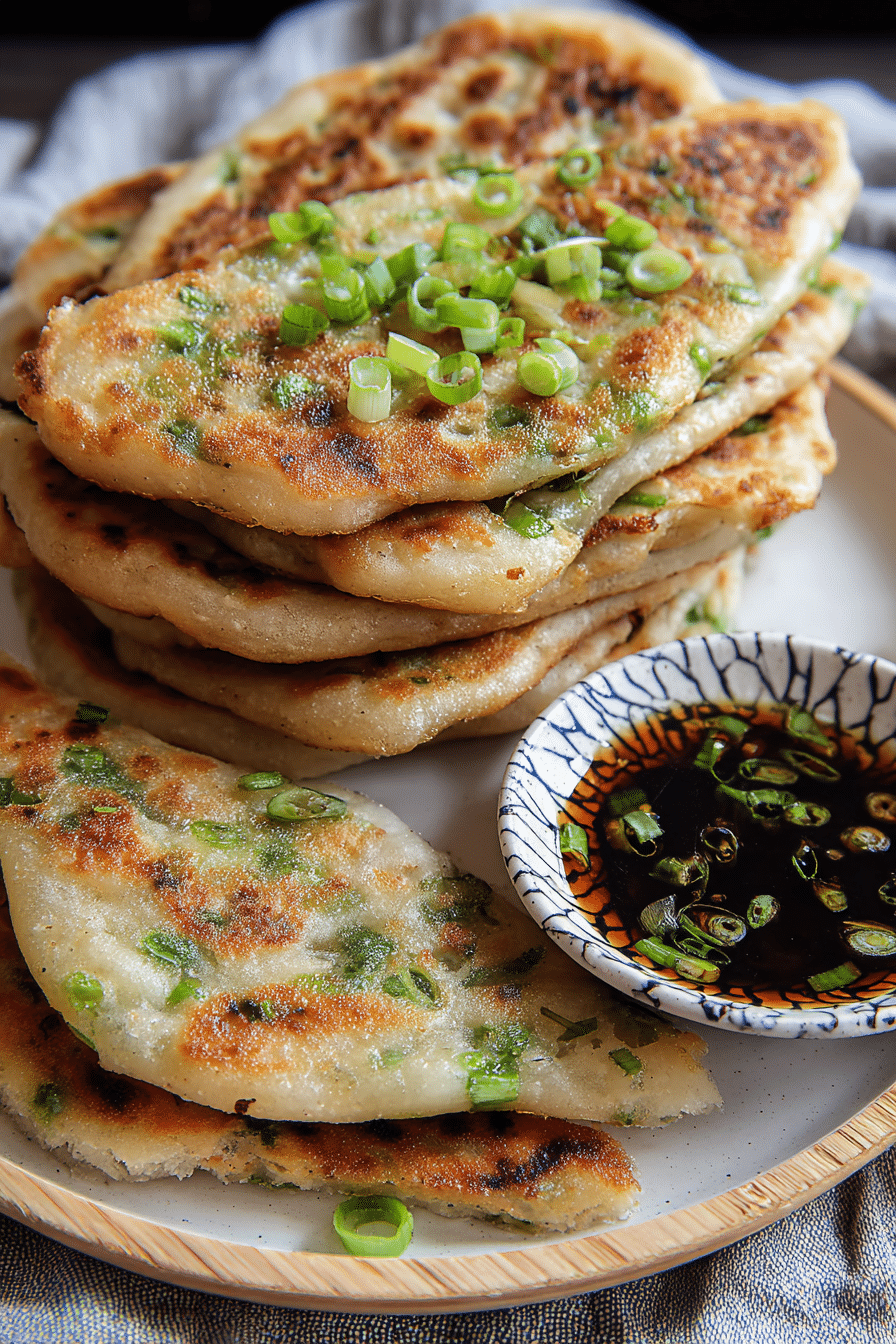 Crispy Chinese scallion pancakes stacked on a plate with scallion garnish and dipping sauce