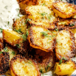 Close-up of crispy parmesan roasted potatoes with herbs and lemon zest on a wooden table.