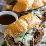 Close-up of a Crockpot French Dip Sandwich with shredded beef, melted cheese, and au jus served on the side.