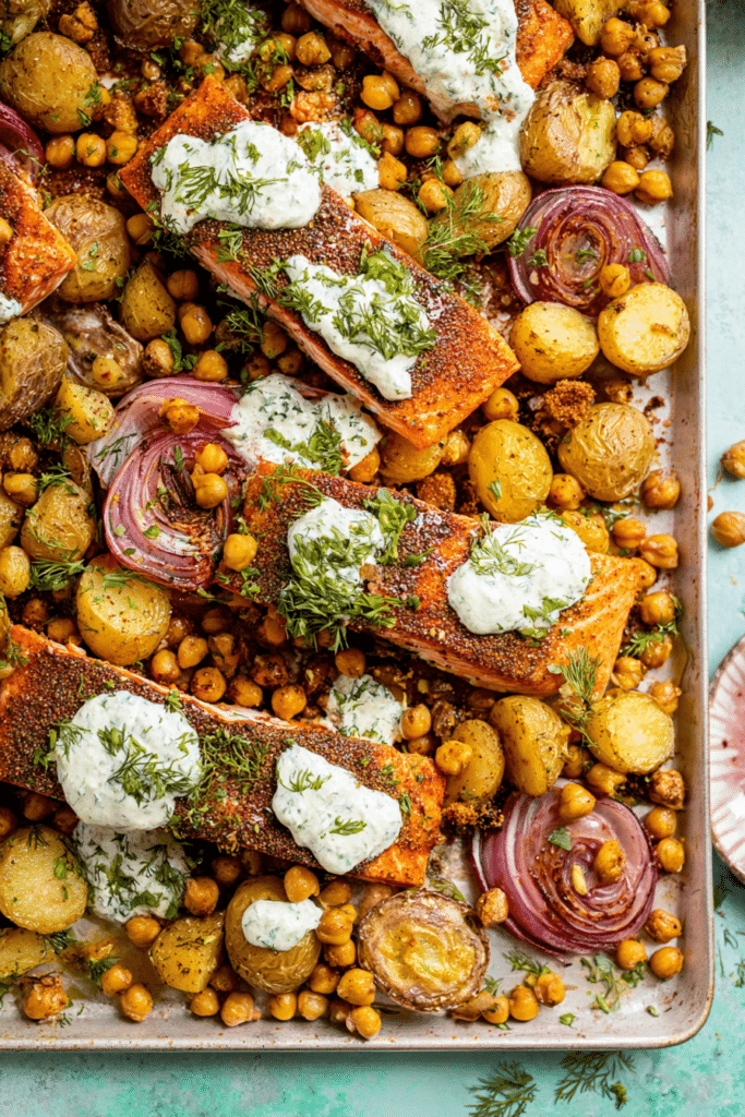 Easy sheet pan salmon dinner with potatoes and chickpeas topped with herby yogurt sauce and fresh herbs