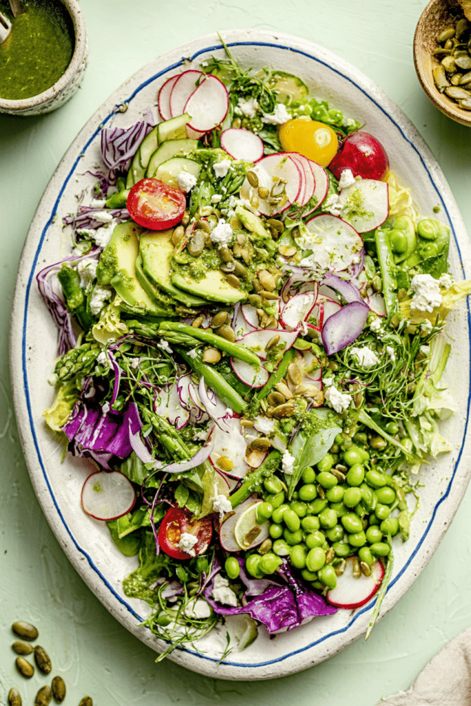 Everything Spring Green Salad with avocado, cherry tomatoes, and lemon basil vinaigrette on a wooden table.