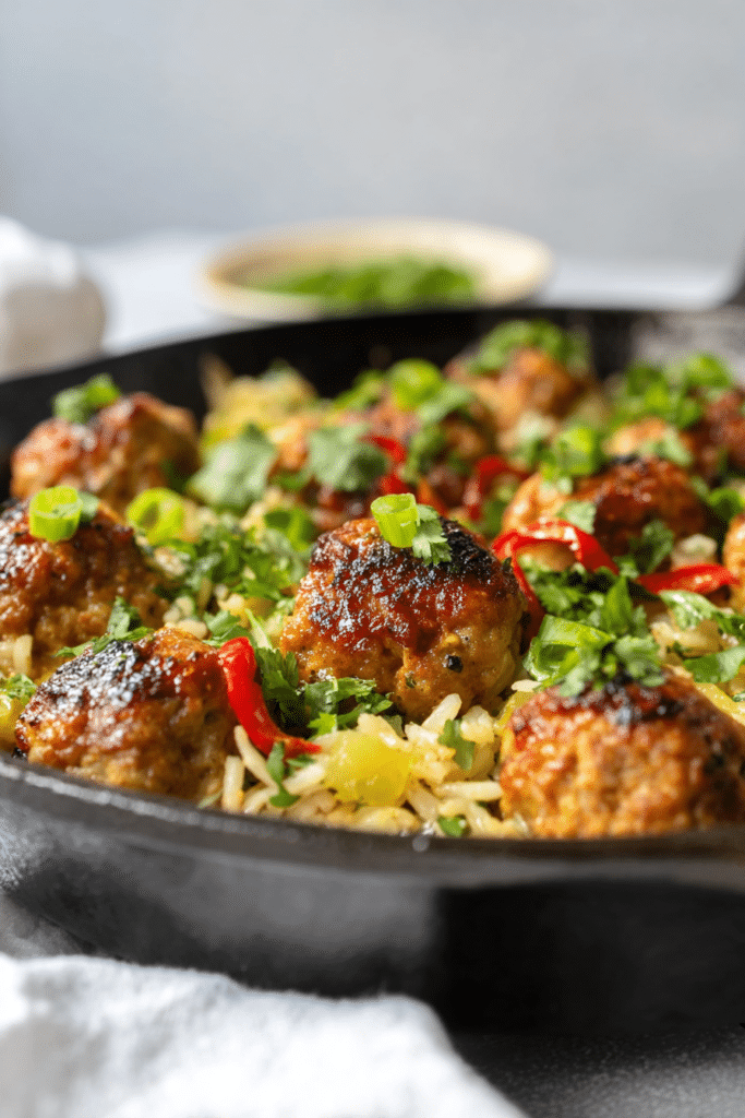 Delicious firecracker chicken meatballs with cilantro coconut pineapple rice, garnished with fresh herbs.