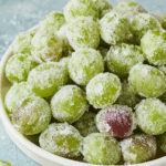 Bowl of sparkling frozen candied grapes with granulated sweetener, showcasing their bright green color and delicious texture.