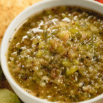 Fresh green tomato salsa in a bowl with tortilla chips and lime slices