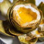 Grilled artichokes with lemon-pepper garlic butter served with lemon wedges and parsley garnish.