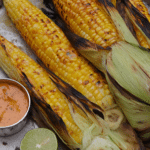 Close-up of grilled corn on the cob with chipotle butter and lime wedges