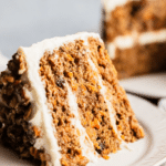 Healthy carrot cake decorated with cream cheese frosting, surrounded by fresh carrots and coconut flakes.