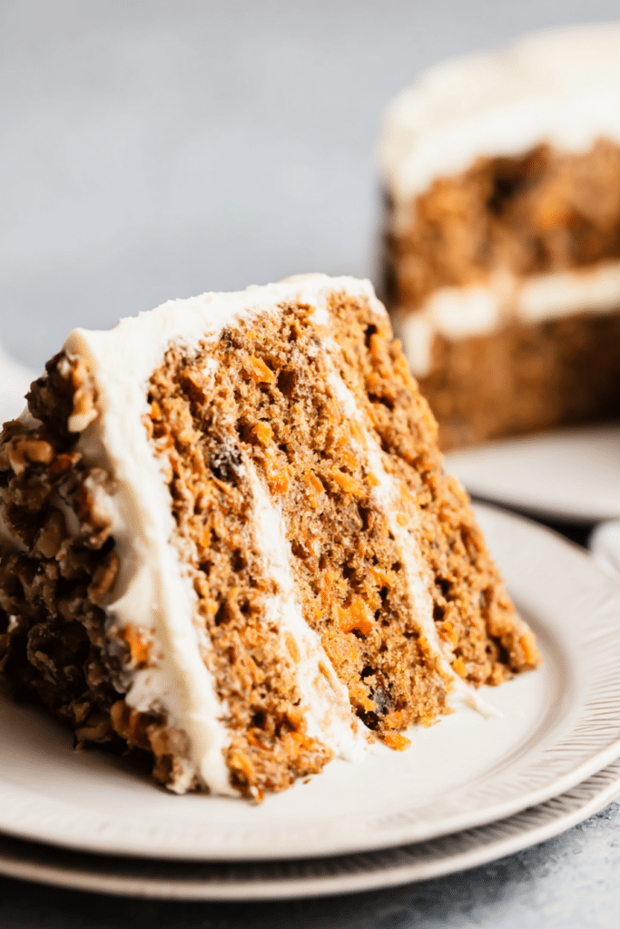 Healthy carrot cake decorated with cream cheese frosting, surrounded by fresh carrots and coconut flakes.