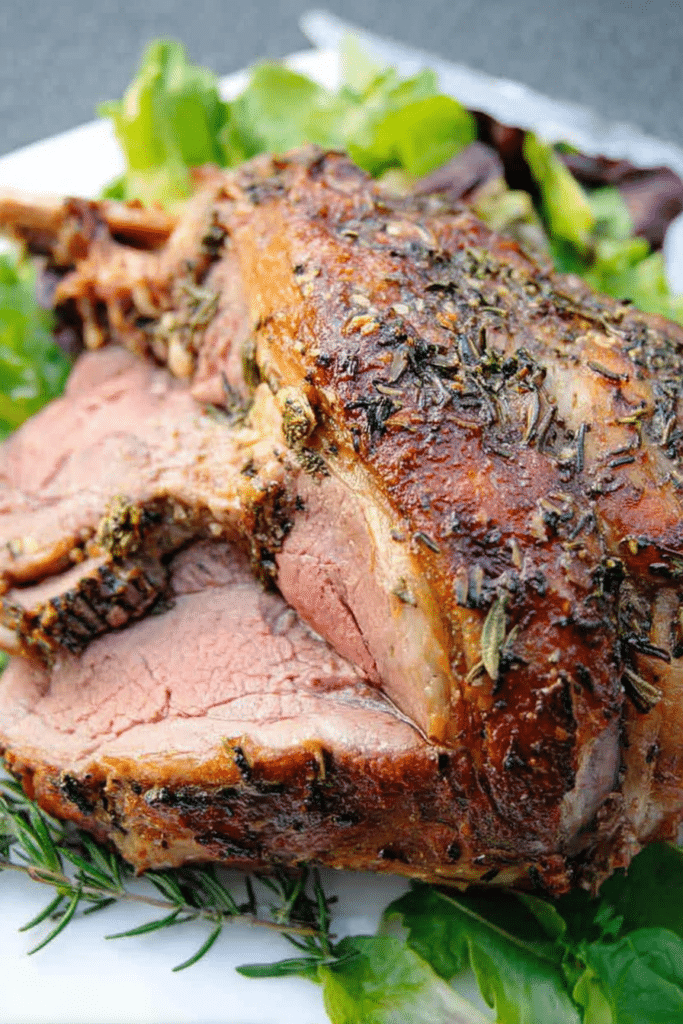 Herb roast leg of lamb garnished with herbs and served with mint jelly on a cutting board.