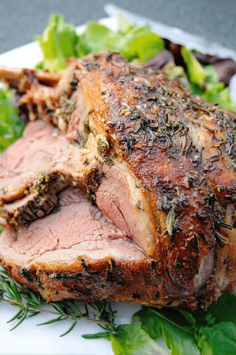 Herb roast leg of lamb garnished with herbs and served with mint jelly on a cutting board.