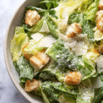 Delicious homemade Caesar salad with croutons and Parmesan cheese on a wooden table.