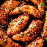 Delicious honey garlic chicken garnished with parsley and sesame seeds on a white plate.