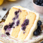 Lemon blueberry cake garnished with blueberries and lemon slices on a rustic wooden table.