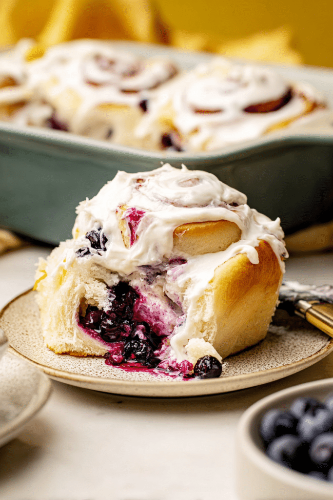 Close-up of a lemon blueberry sweet roll with lemon cream cheese frosting and fresh blueberries.