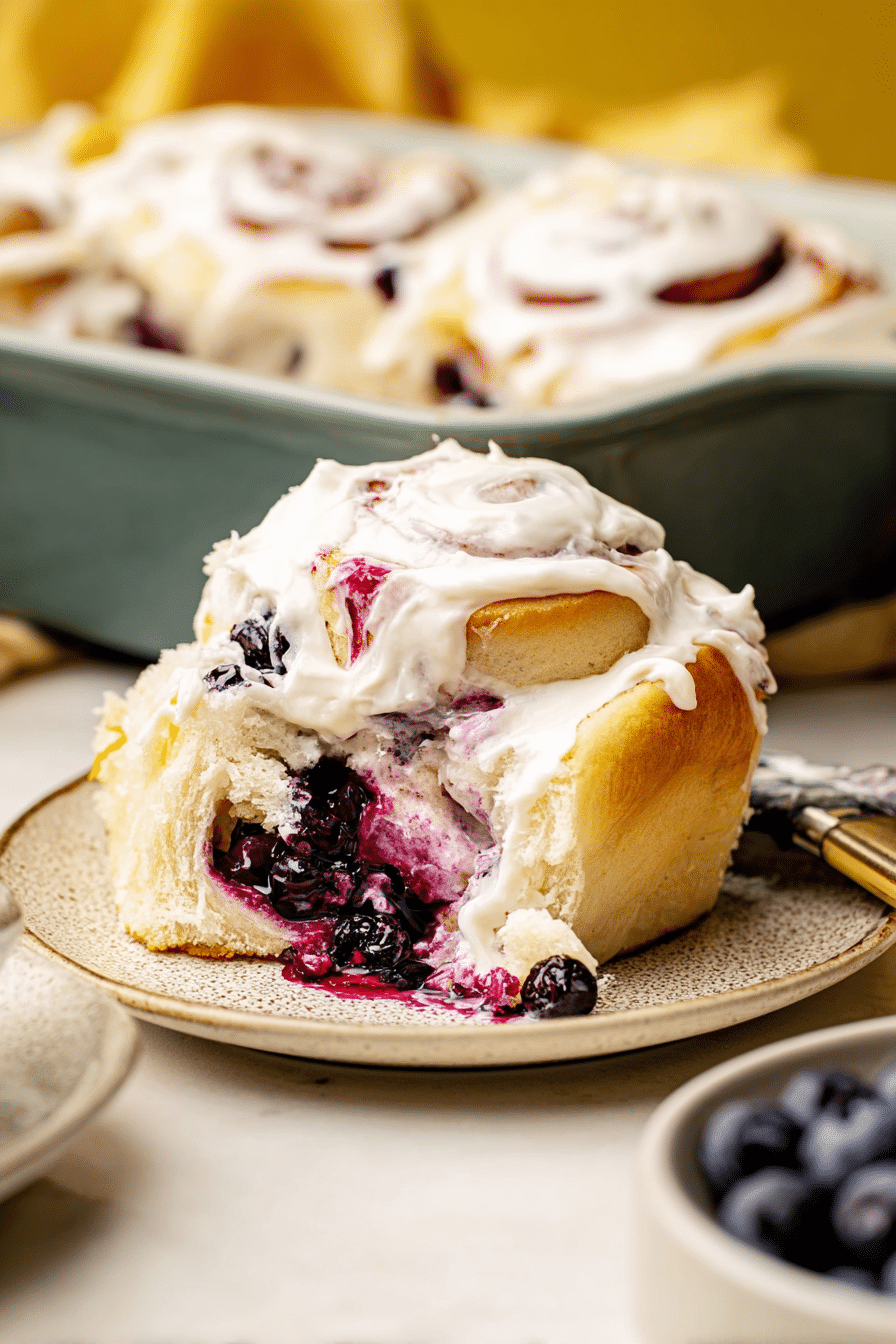 Close-up of a lemon blueberry sweet roll with lemon cream cheese frosting and fresh blueberries.