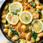 Close-up of lemon chicken gnocchi with parmesan cheese, lemon slices, and fresh spinach in a bowl.
