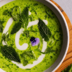 A colorful bowl of nettle soup with microgreens and edible flowers, served with rustic bread.