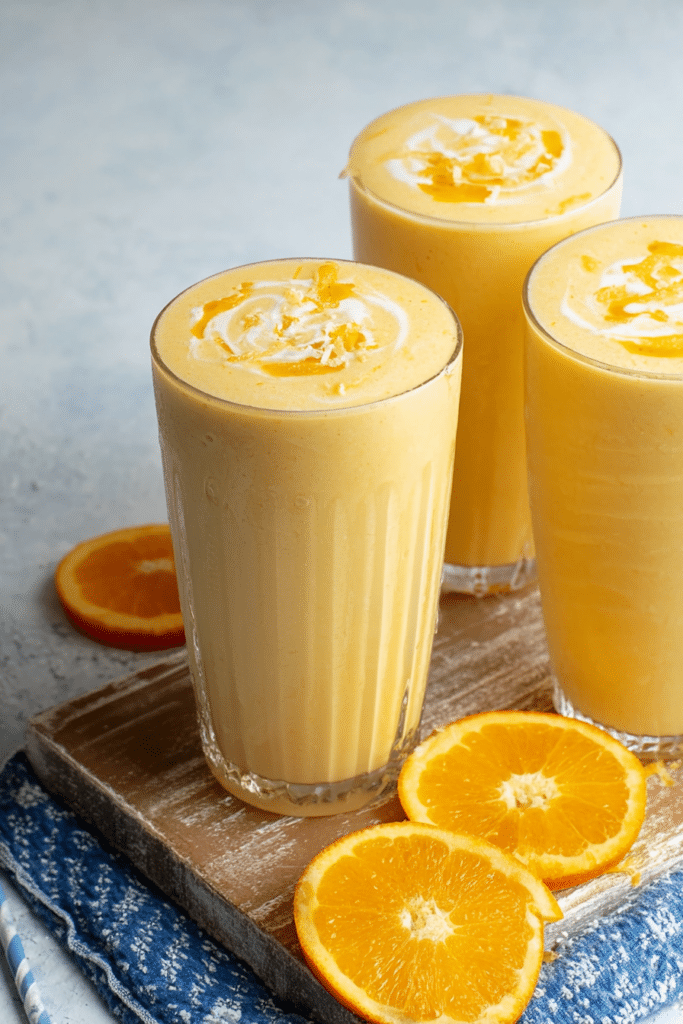 Refreshing orange creamsicle smoothie in a tall glass with orange garnish on a wooden table