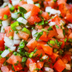Fresh pico de gallo salsa made with diced tomatoes, onions, jalapenos, and cilantro in a bowl with a lime wedge.