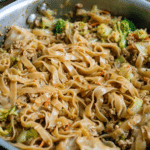 Delicious potsticker bowl with rice noodles, ground pork, and fresh vegetables garnished with green onions and red pepper flakes.