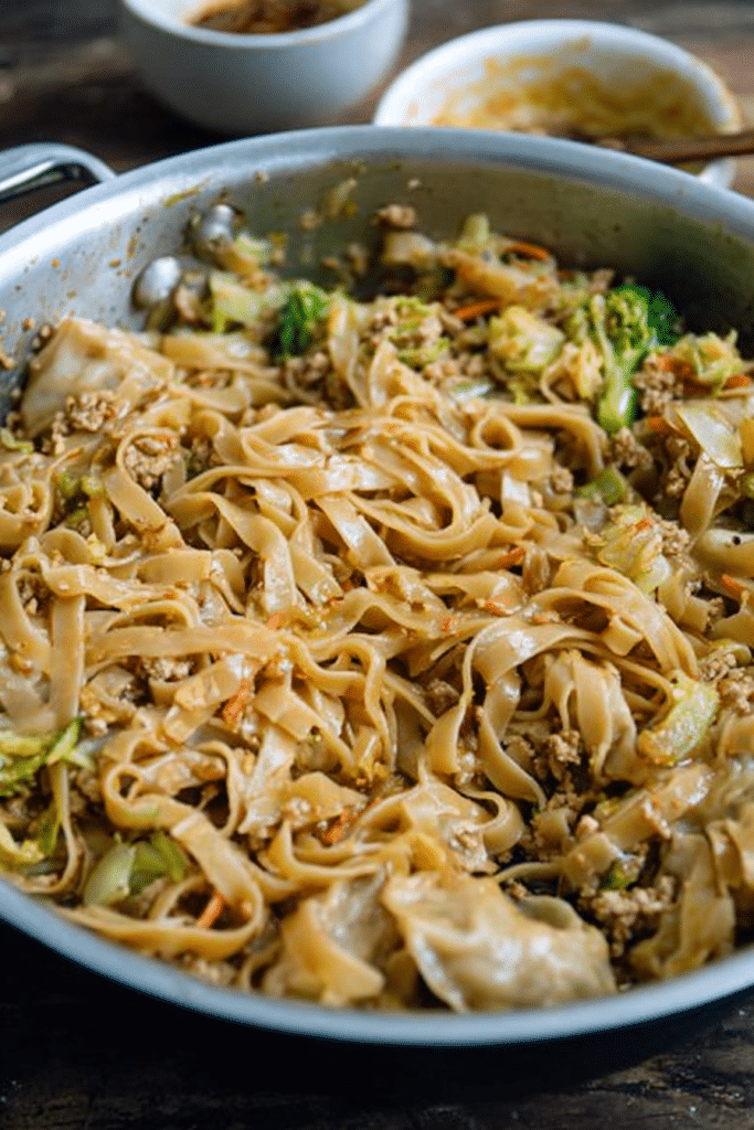 Delicious potsticker bowl with rice noodles, ground pork, and fresh vegetables garnished with green onions and red pepper flakes.