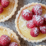 Close-up of a raspberry lemon tart topped with fresh raspberries and powdered sugar on a wooden table