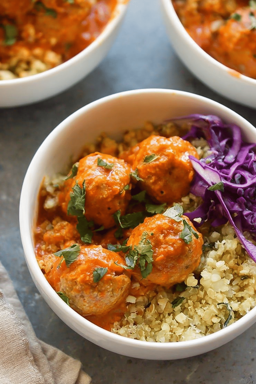 Red coconut curry meatballs served with cauliflower rice, garnished with cilantro and lime, capturing the essence of Thai cuisine.