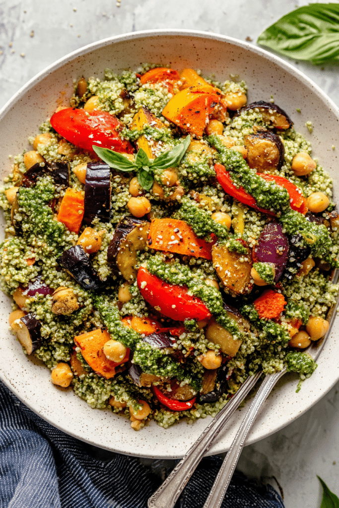 A colorful roasted veggie chickpea pesto quinoa salad topped with fresh basil and lemon slices.