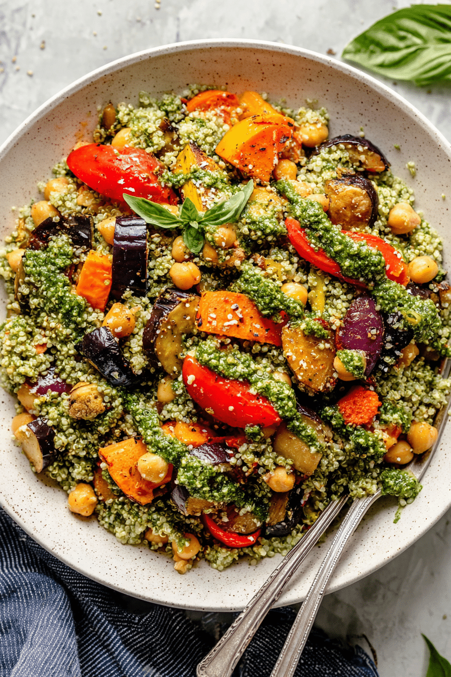 A colorful roasted veggie chickpea pesto quinoa salad topped with fresh basil and lemon slices.
