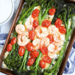 Sheet pan shrimp with broccolini and tomatoes, featuring roasted shrimp, green broccolini, and halved grape tomatoes on a rustic wooden table.