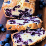 Sliced blueberry cream cheese bread on a cutting board with fresh blueberries