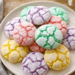 A plate of vibrant springtime crinkle cookies topped with powdered sugar, surrounded by pastel Easter decorations.