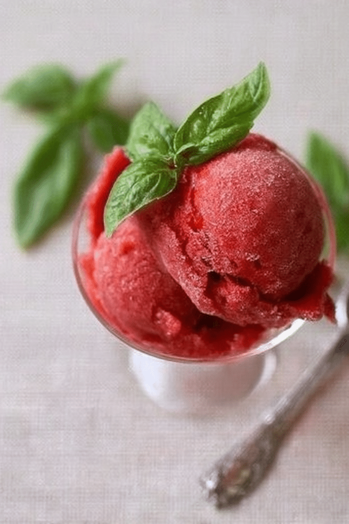 Strawberry basil sorbet served in a bowl with fresh basil leaves on top.