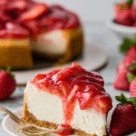 Slice of strawberry cheesecake garnished with fresh strawberries on a white plate