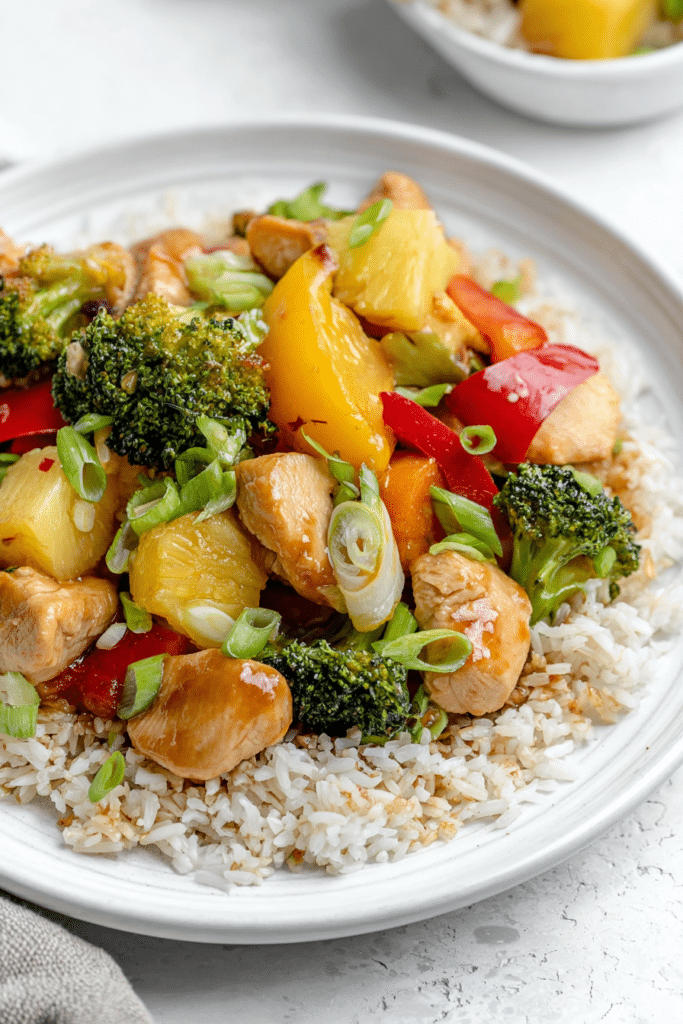 Sweet and sour pineapple broccoli chicken stir fry with chicken, broccoli, and pineapple in a bowl, topped with scallions.