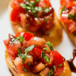 Delicious homemade tomato bruschetta with fresh basil on a wooden platter, drizzled with balsamic glaze.