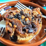 Delicious serving of traditional Mexican capirotada bread pudding topped with melted cheese, raisins, and nuts.