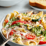 Vegan pasta primavera topped with creamy garlic cashew sauce and fresh vegetables, including zucchini, broccoli, and cherry tomatoes.