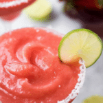 Vibrant frozen strawberry margarita cocktail with fresh strawberries and lime slice garnishes on a sunny patio
