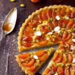 Apricot Crème Fraîche Tart topped with honey and pistachios served on a rustic wooden table.