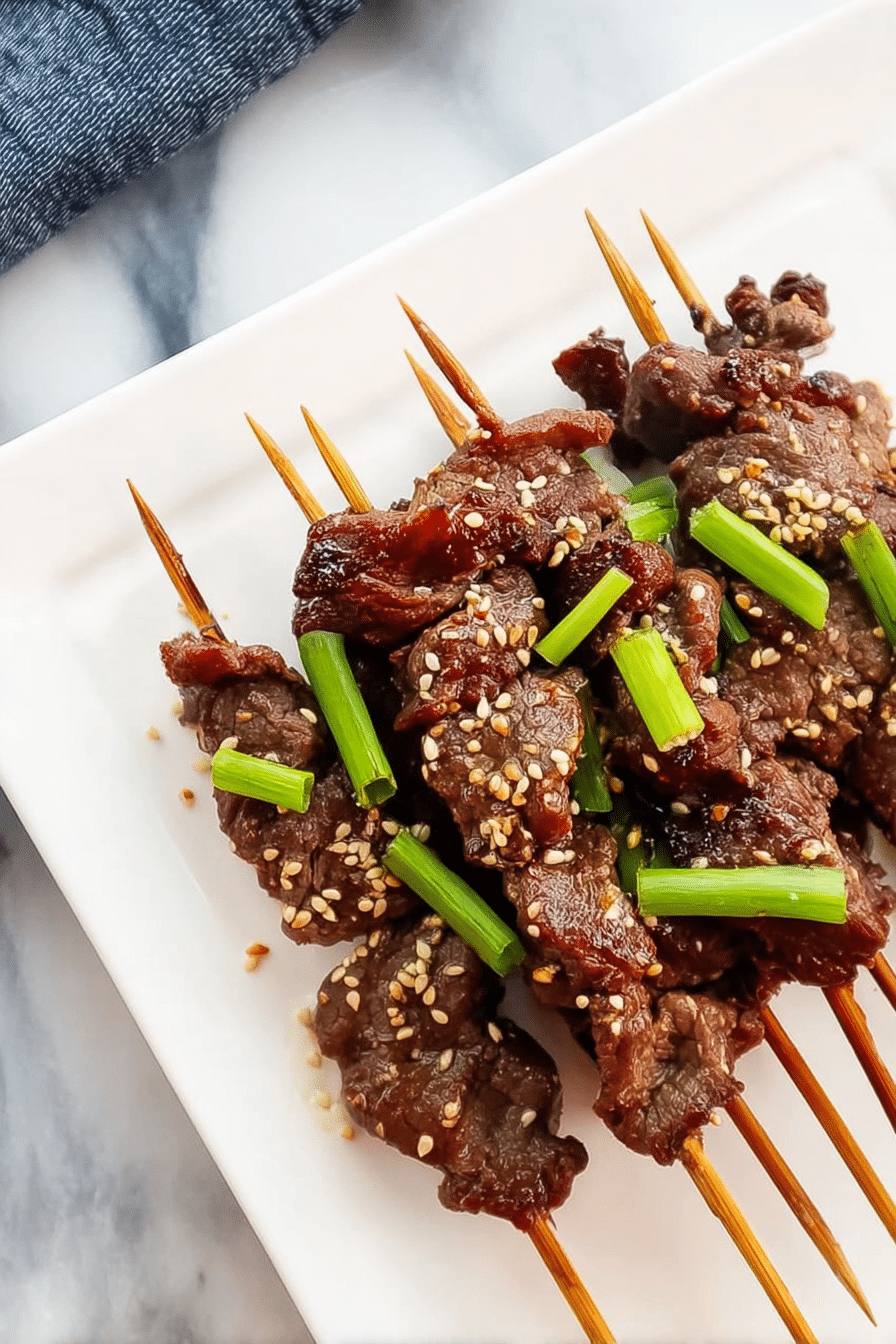 Grilled Asian sesame beef skewers garnished with sesame seeds and green onions on a wooden board with dipping sauce.