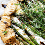 Asparagus galette with jammy leeks and ricotta on a rustic wooden table, garnished with herbs.
