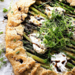 Asparagus galette with jammy leeks and ricotta on a rustic wooden table, showcasing the golden crust, vibrant asparagus, and creamy ricotta.